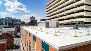 Commercial roofing view with flat white surface, surrounded by urban buildings and a parking structure, highlighting roofing maintenance importance.