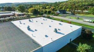 Aerial view of a commercial building roof with white flat roofing, showcasing HVAC units and surrounding greenery, relevant to roofing maintenance and services by J.B. Miller Contractors.