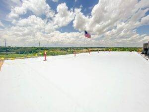 Flat commercial roof with white coating, American flag waving, and a scenic view of green landscape and cloudy sky, relevant to roofing materials and performance discussion.